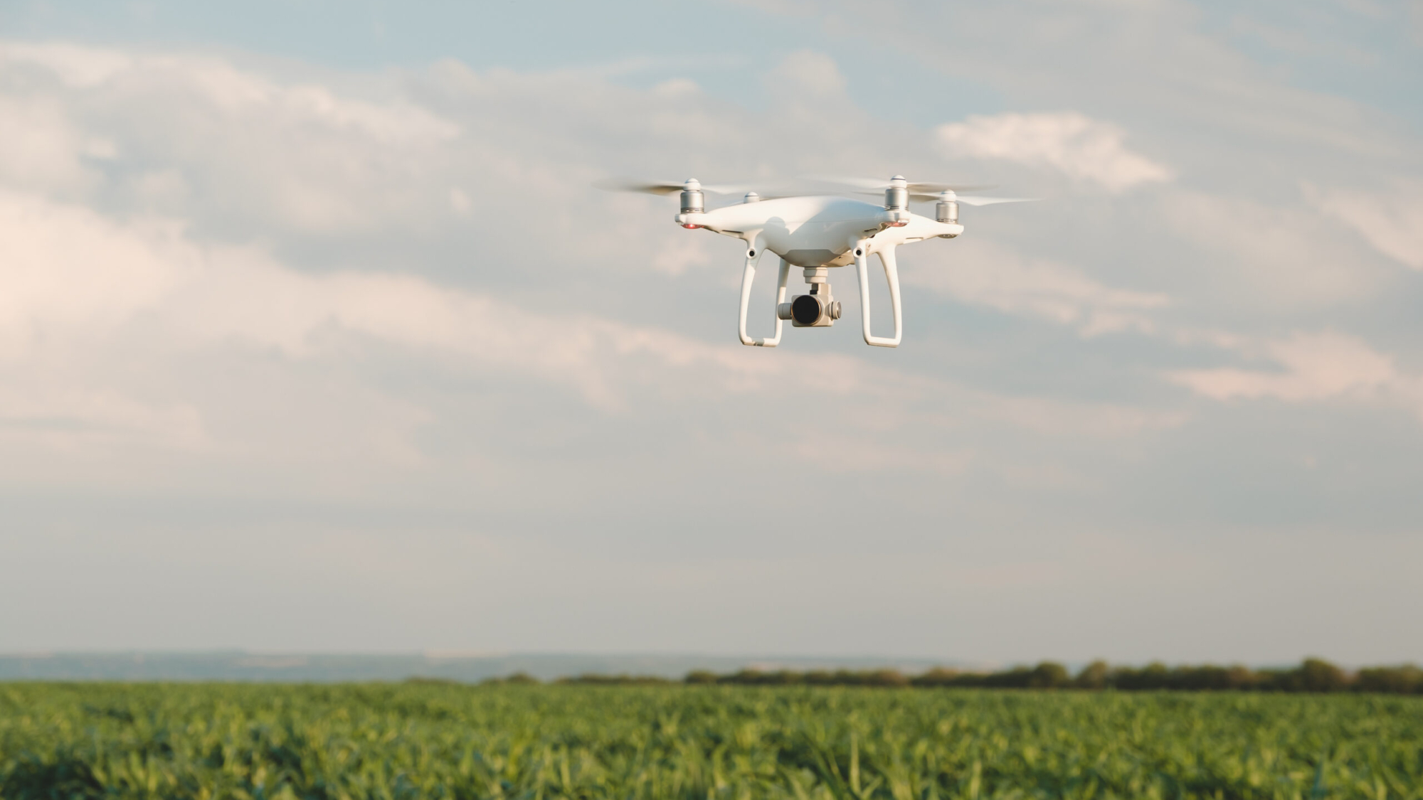 White drone hovering in a bright blue sky. Drone copter flying with digital camera