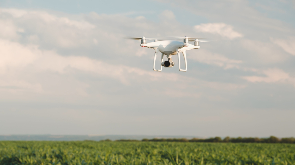 White drone hovering in a bright blue sky. Drone copter flying with digital camera