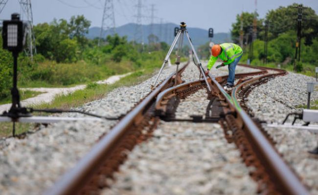 Engineer wearing hard hats and uniforms use theodolite equipment surveying construction worker on Railway site.